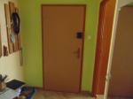 Przedpokój utrzymany w pastelowych kolorach zieleni i kremu, jasnobrązowe drzwi wyjściowe na wprost, po lewej stronie wieszaki na odzież zewnętrzną, po prawej szafa z lustrem, za szafą wejście do pomieszczenia